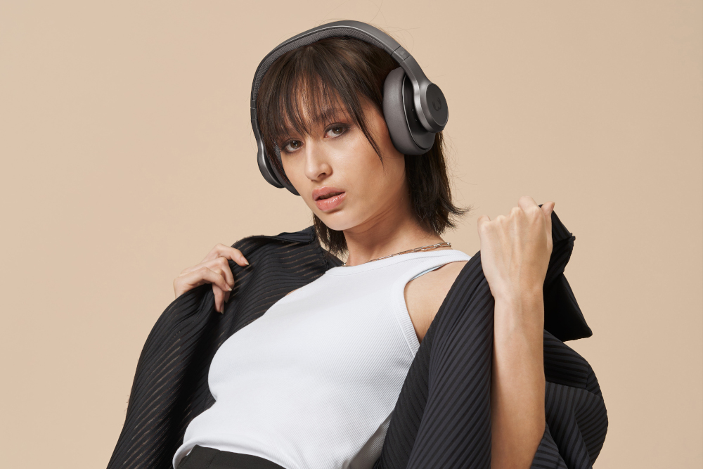Une femme portant un casque, un haut blanc et une veste noire, posant sur un fond marron clair.