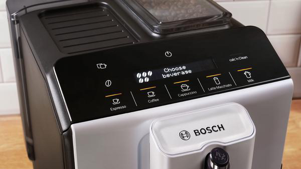 Eine Bosch-Kaffeemaschine mit schwarz-silbernem Design. Sie hat einen Bildschirm und Tasten zur Getränkeauswahl. Die Front hat einen weißen Bereich.