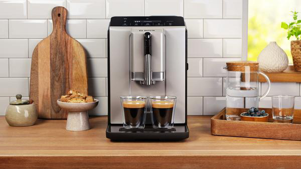 Eine Kaffeemaschine mit zwei Espressotassen, Schneidebrett, Snacks und einem Tablett mit Wasser und Blaubeeren.