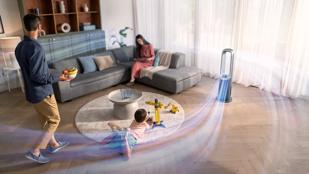 Család a nappaliban; férfi gyümölccsel, nő a kanapén, gyerek játékkal, ventilátor jobbra.