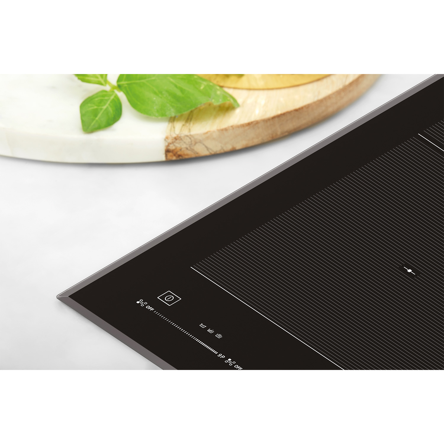 Primo piano di un piano cottura nero con tagliere in legno e foglie di basilico.