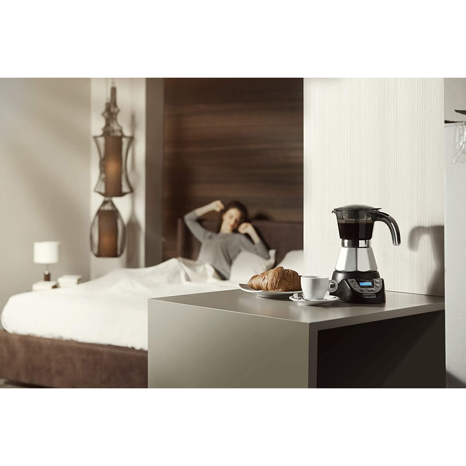 Caffettiera su un tavolo, una donna a letto sullo sfondo.