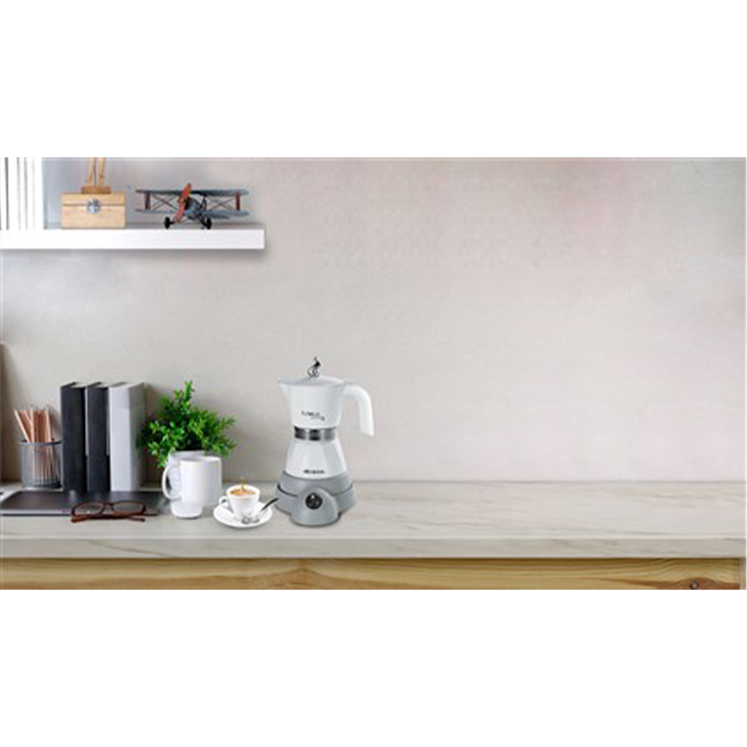 Una caffettiera elettrica bianca e grigia con una tazza e un piattino su un tavolo.