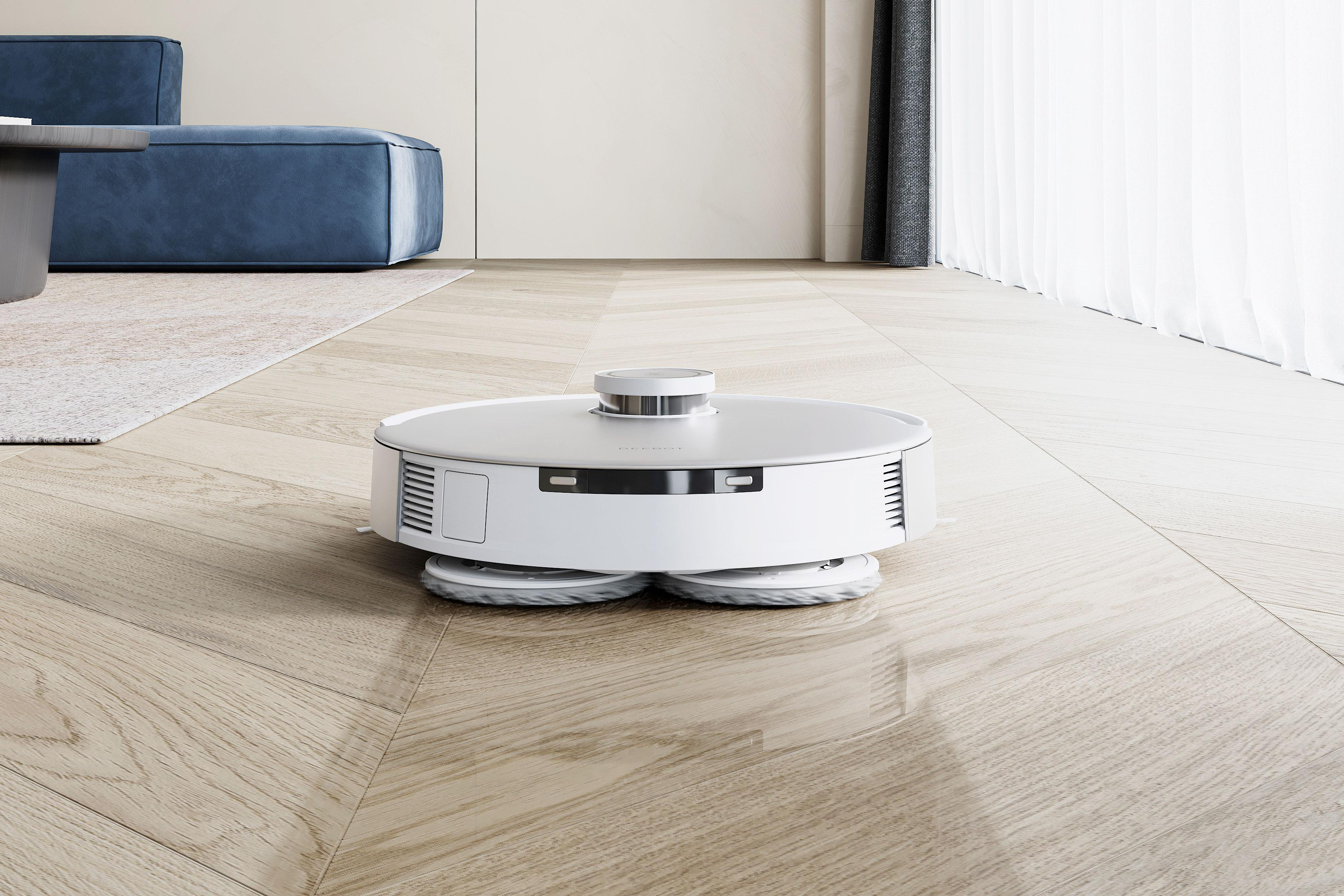Ein weißer Roboter-Staubsauger auf einem Holzboden. Im Hintergrund befindet sich ein blaues Sofa.