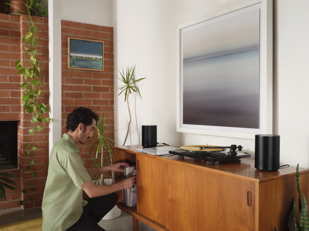 Man arranging books next to two black speakers and a turntable on wooden cabinet.