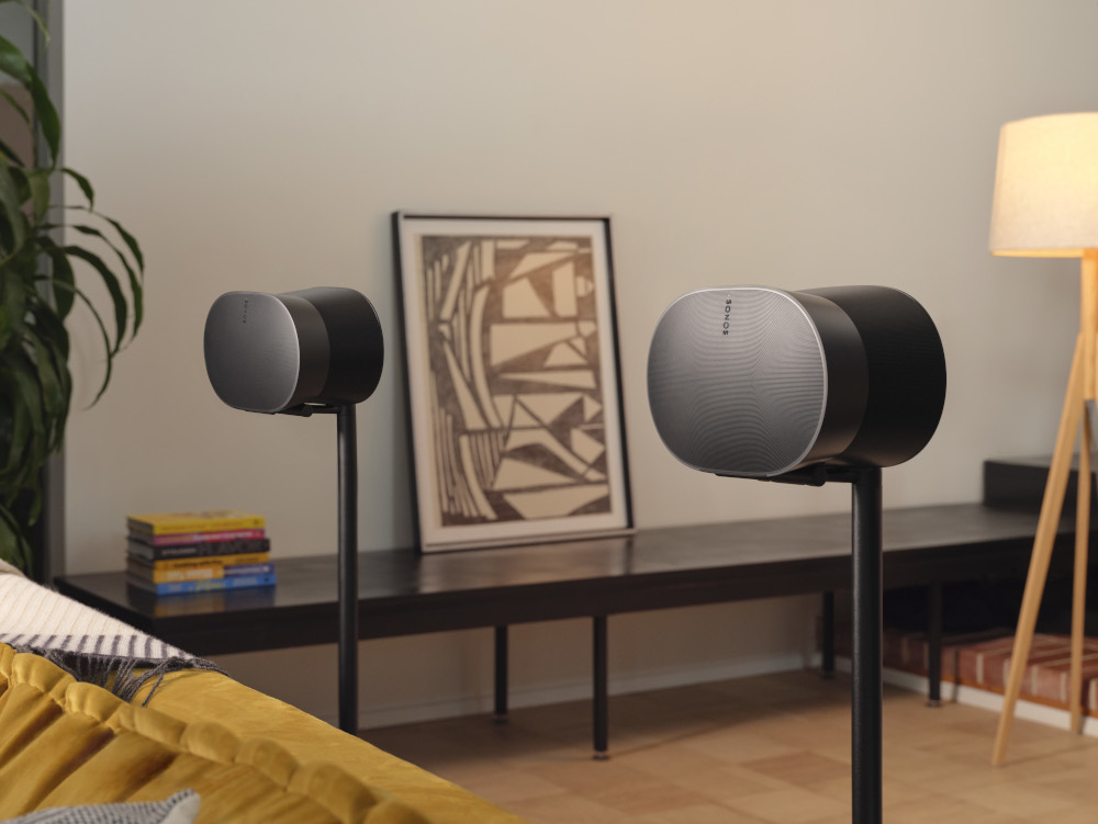 Two black speakers on stands, a framed picture, and a yellow sofa in a room.