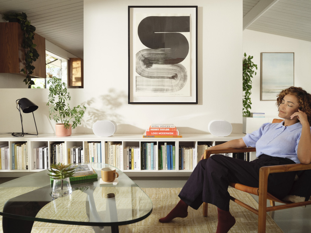 Woman sitting in a chair listening to music with two white speakers on a shelf.