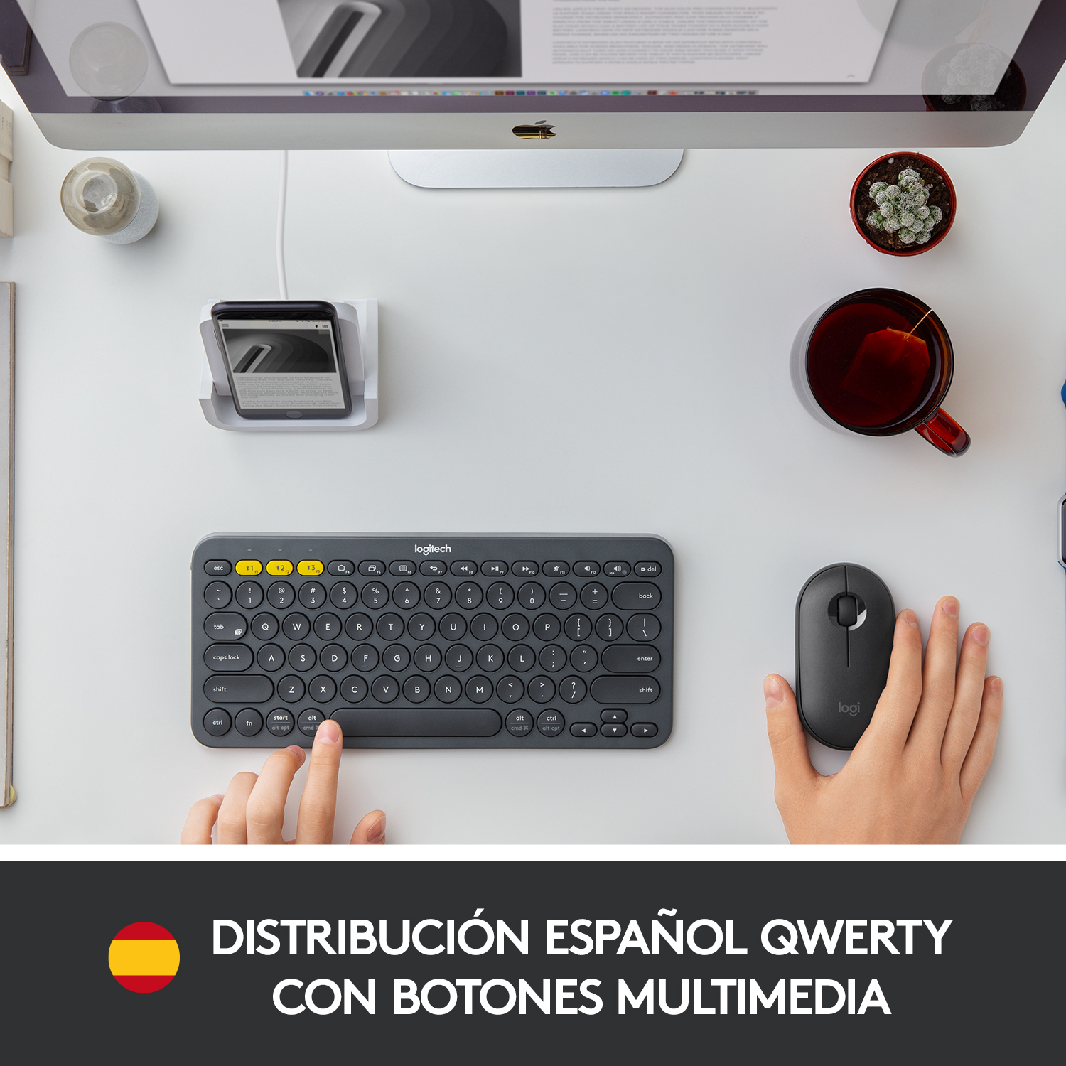 Configuración de escritorio: teclado, ratón, teléfono, taza de té, planta pequeña. Manos interactuando con teclado y ratón.