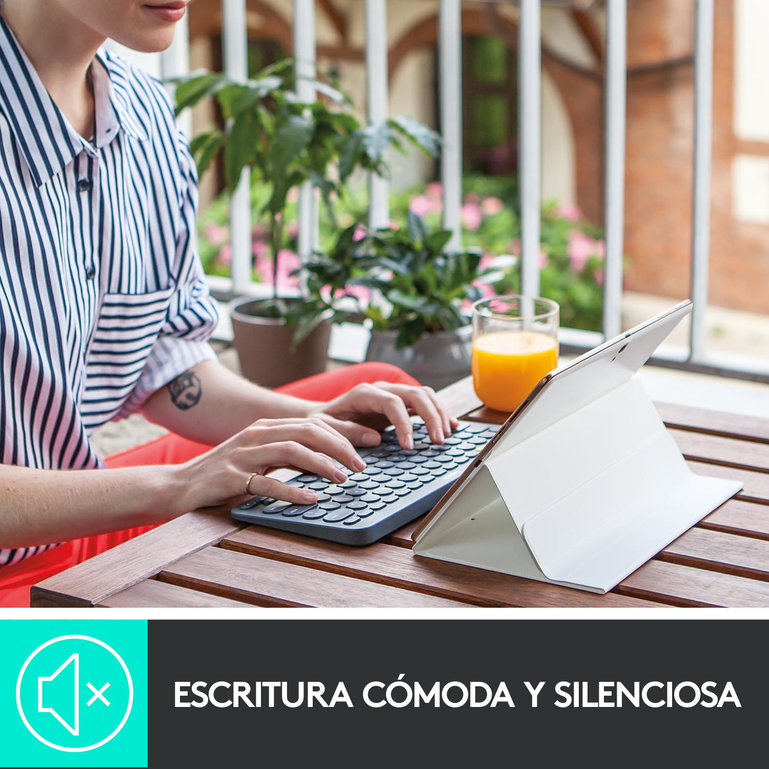 Una mujer escribiendo en un teclado, una tableta y un vaso de zumo.