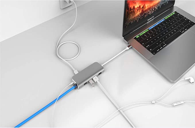 Ordenador portátil conectado a un concentrador con varios cables y un auricular blanco.