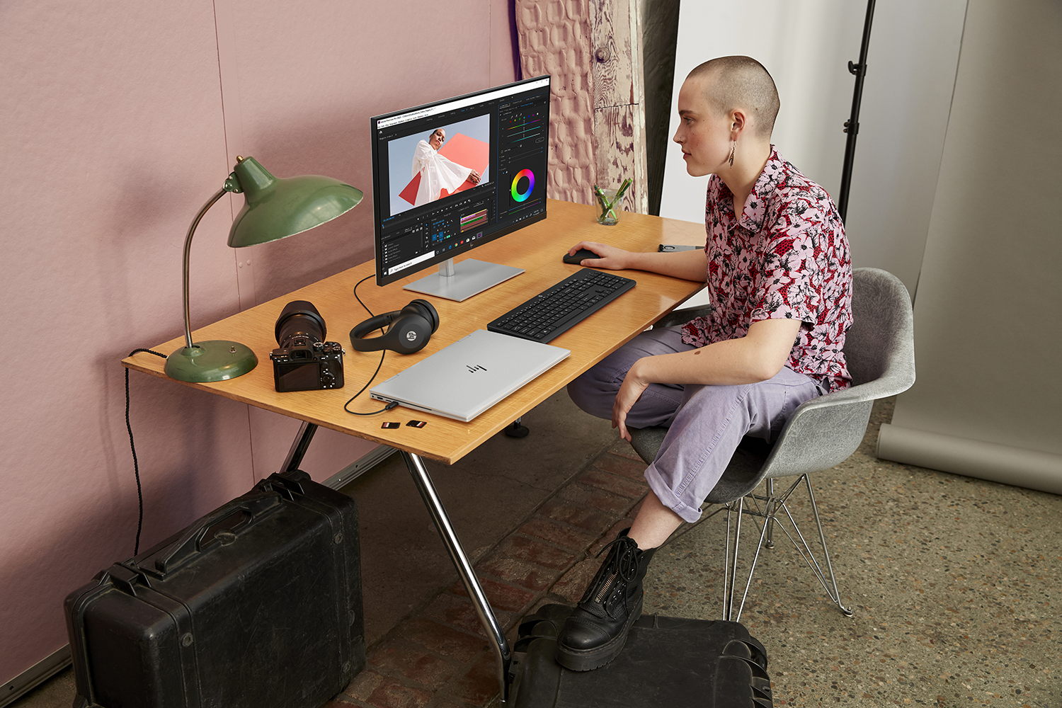 Persoon aan bureau met computer, camera en koptelefoon. Bewerkingssoftware weergegeven op het scherm.