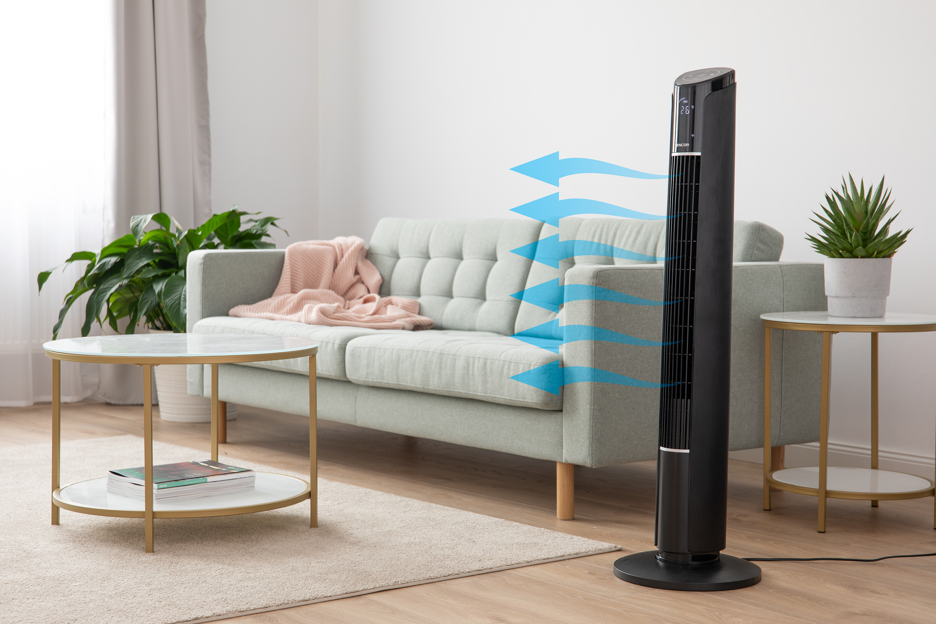 Nappali fekete ventilátorral, ami levegőt fúj. Látható még egy kanapé, asztalok és növények.