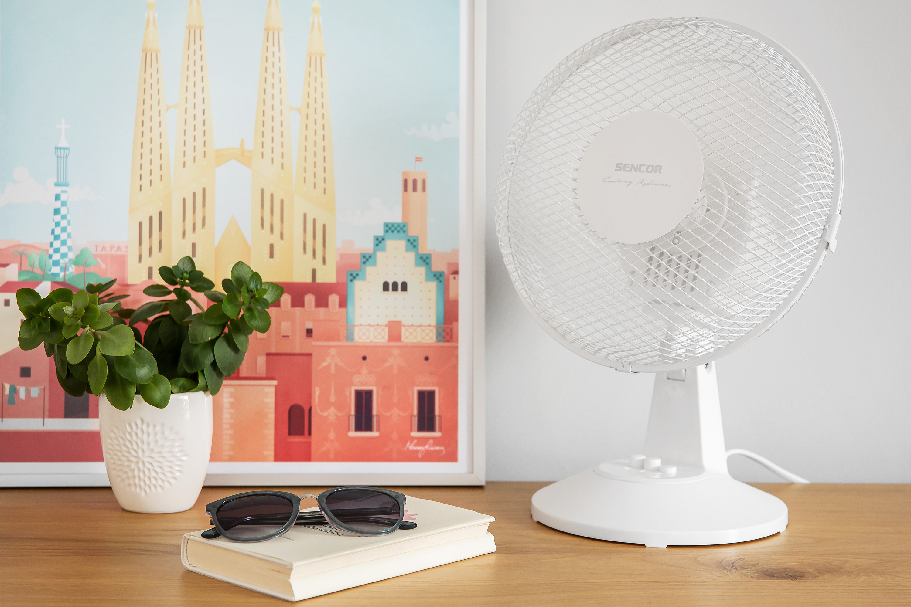 Fehér asztali ventilátor egy képpel és napszemüveggel egy fa felületen.