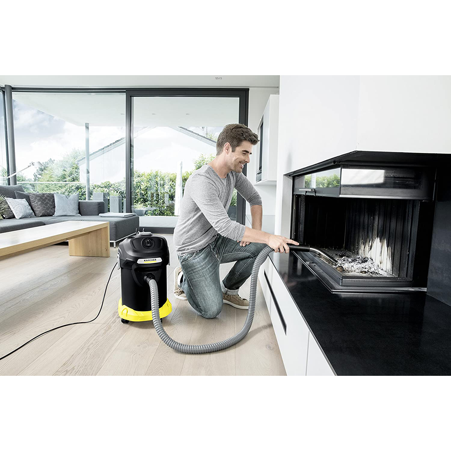 Uomo che aspira il camino, con un aspirapolvere Karcher, in un moderno soggiorno con una grande finestra.