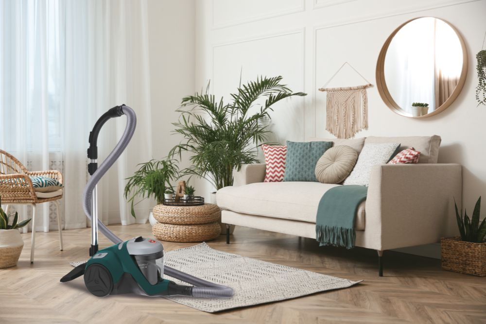 Wohnzimmer mit Staubsauger auf dem Boden. Beiges Sofa, Holzboden, Pflanzen.