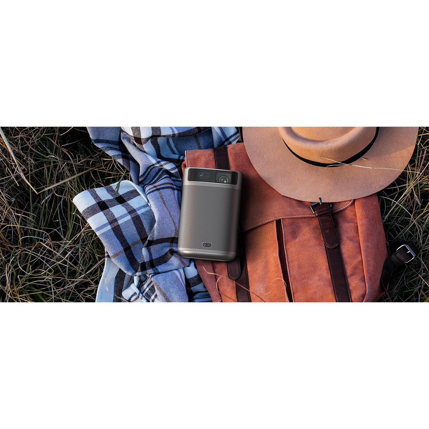 Un proiettore portatile grigio con uno zaino, un cappello e una coperta sull'erba.
