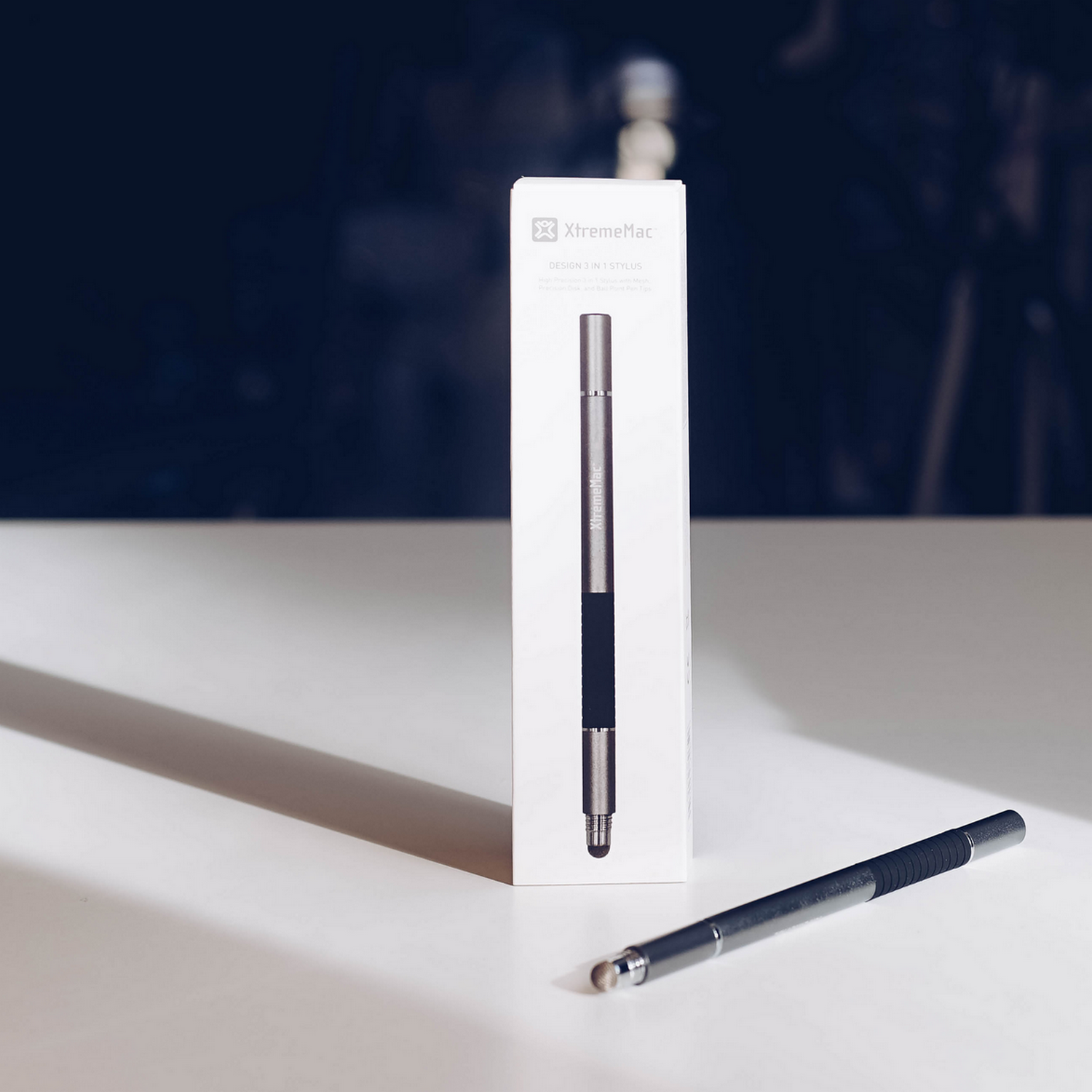 Stylus and its box on a white surface. The box reads 'XtremeMac'. Dark blue background.