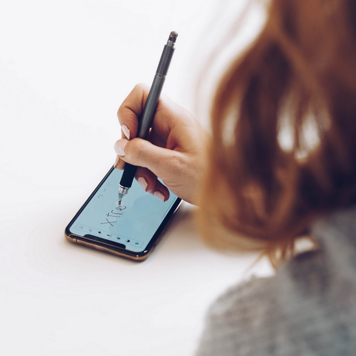 Hand with pen writing on phone screen. White background.