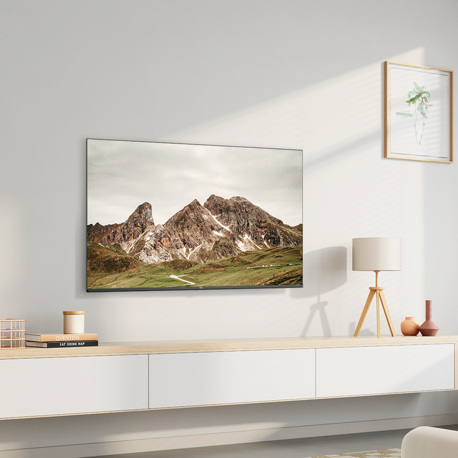 Een tv aan een witte muur. Een berglandschap staat op het scherm. Een lamp en decoratie zijn aanwezig.