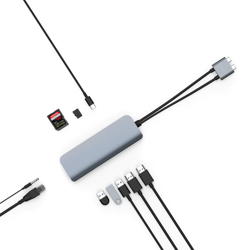 Un hub USB-C gris con múltiples cables y conectores adjuntos sobre una superficie blanca.