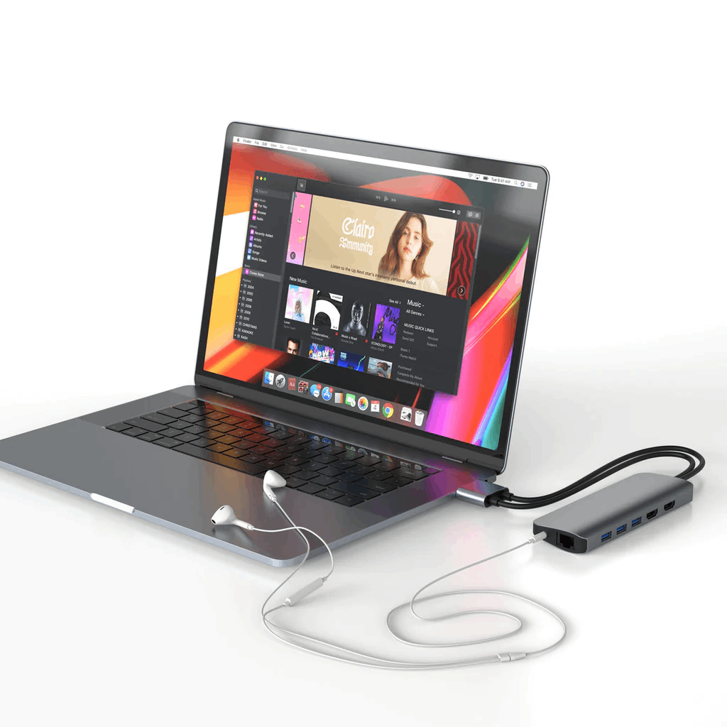 Laptop con un concentrador conectado. El portátil muestra una aplicación de música. Auriculares blancos enchufados.