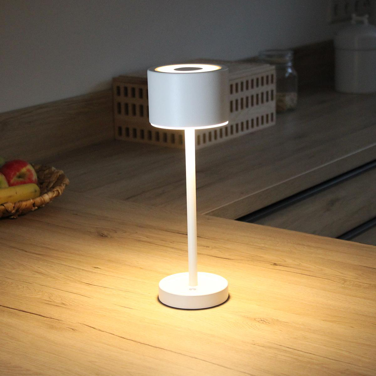 Eine weiße Nachttischlampe auf einer hölzernen Arbeitsplatte, beleuchtet.