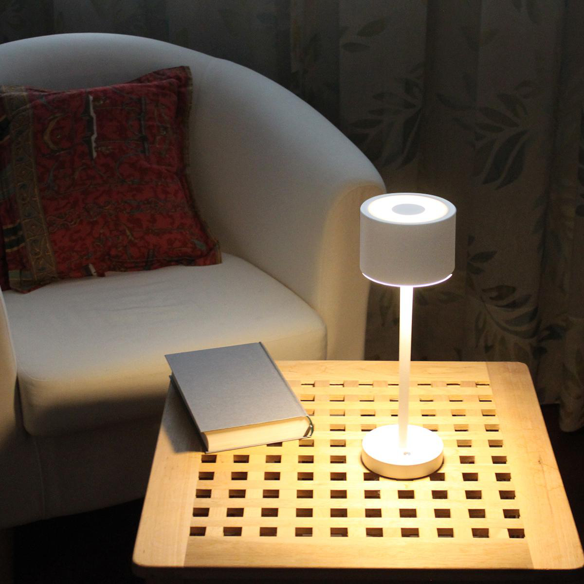 Weiße Lampe auf einem Holztisch, mit Buch und Stuhl. Die Lampe scheint nach unten.