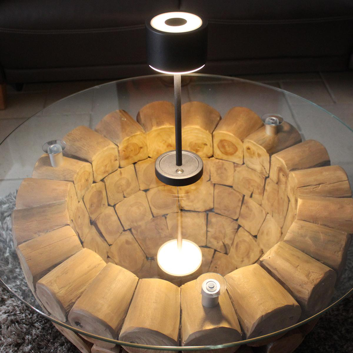 Eine moderne Lampe auf einem Glastisch mit Holzsockel und einem Teppich.