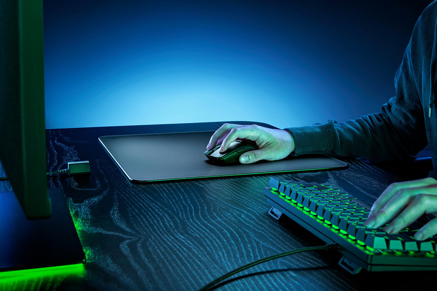 Mains d'une personne utilisant une souris et un clavier sur un bureau. Le clavier brille en vert.