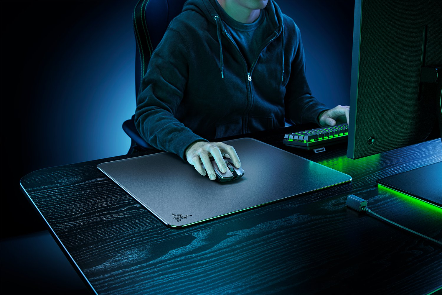 Une personne utilise une souris sur un bureau de jeu, avec clavier et moniteur visibles. Fond sombre.