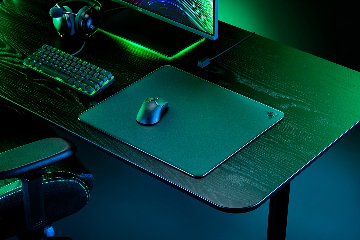 Une configuration de jeu sur un bureau noir. Clavier, souris sur un tapis, casque et un moniteur.