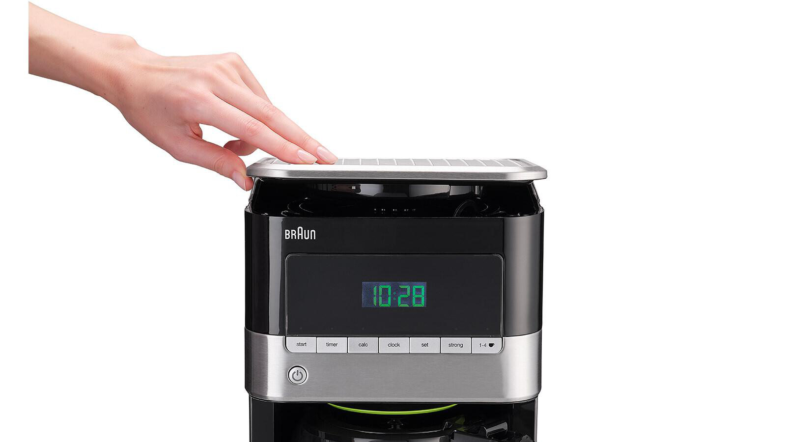 Eine Hand drückt eine Taste auf einer schwarzen Kaffeemaschine mit Digitalanzeige.