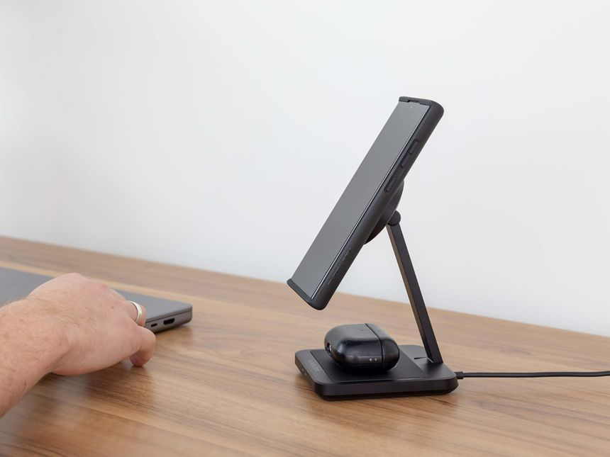 Smartphone su un supporto nero con AirPods. Una mano si protende verso il laptop.