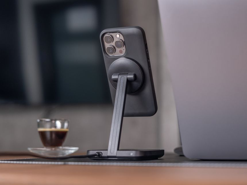 Telefono nero su supporto vicino a laptop e tazza di caffè.