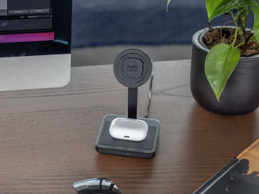 Caricabatterie wireless con base di ricarica bianca e supporto nero, una pianta, un mouse e una scrivania.