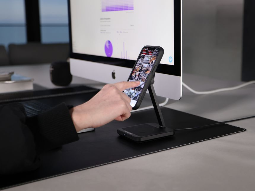 Una persona usa uno smartphone su un supporto su una scrivania con un monitor.