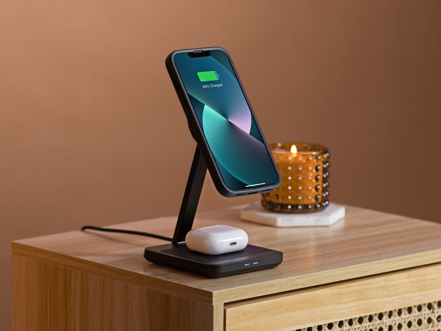 Un telefono in carica su un supporto con una candela e una superficie in legno.