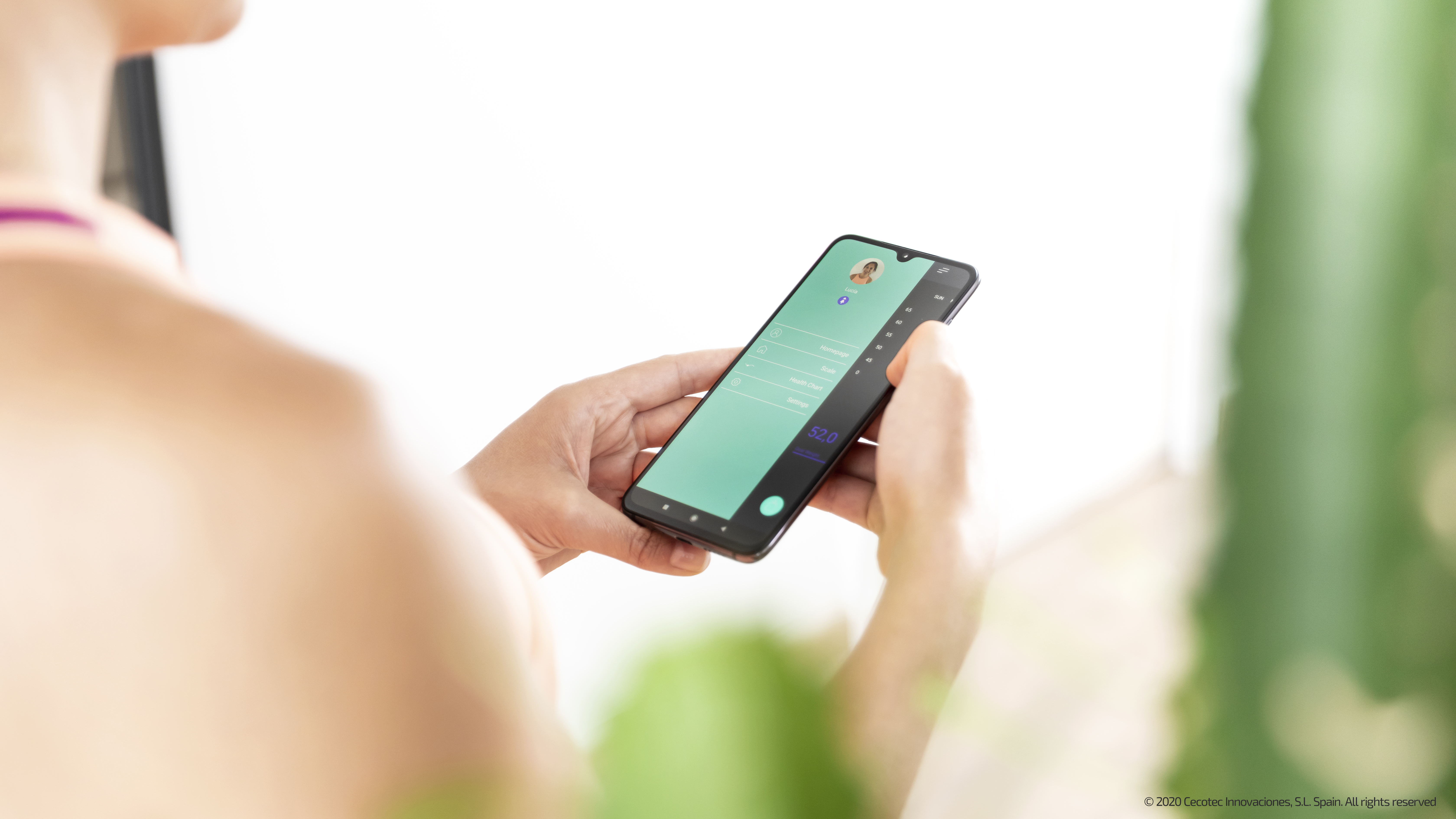 Persona sosteniendo un teléfono con pantalla verde azulado. La pantalla muestra una interfaz de usuario.
