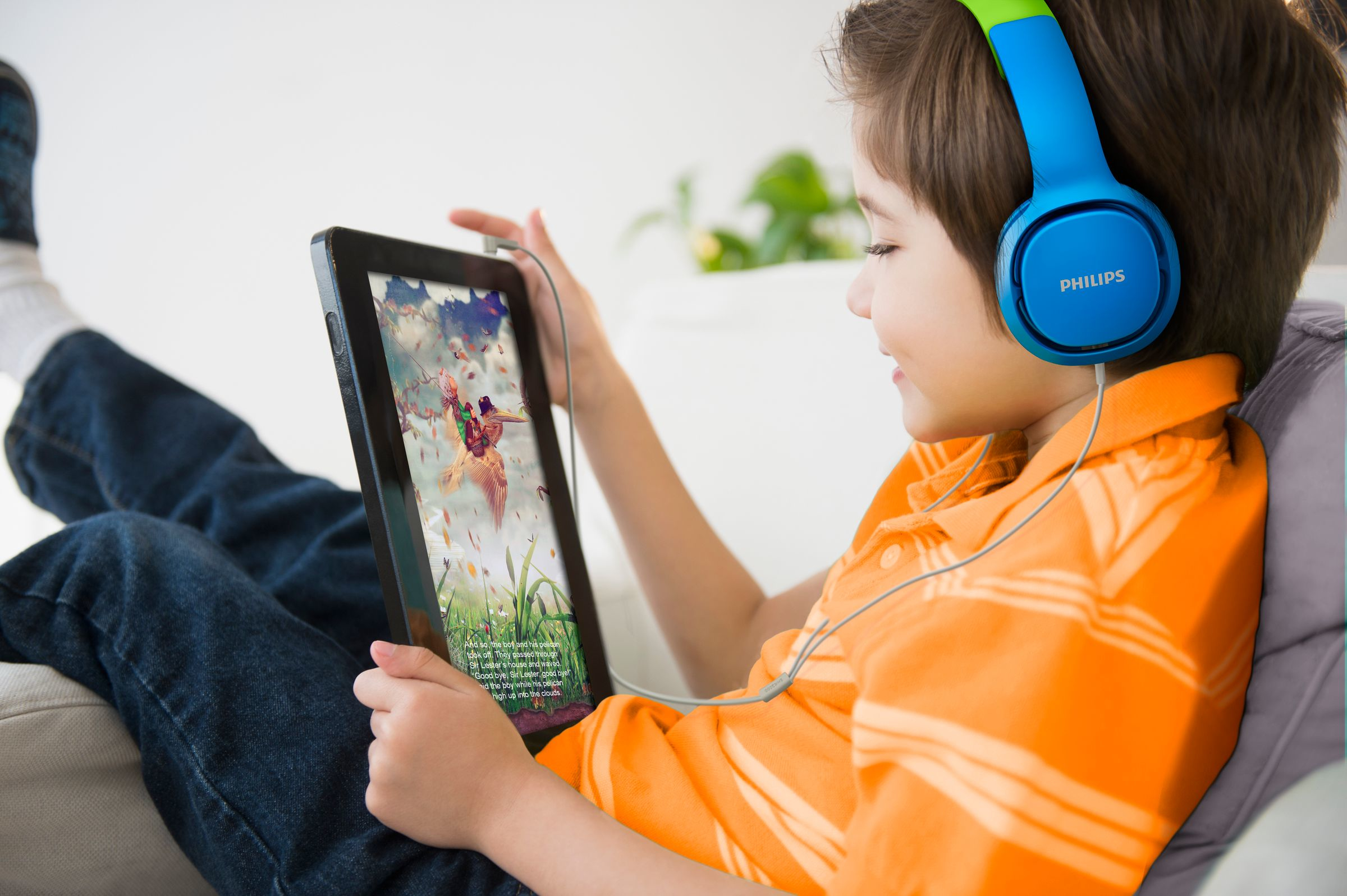 Een jongen met een blauwe koptelefoon kijkt naar een tablet, met een cartoon op het scherm.