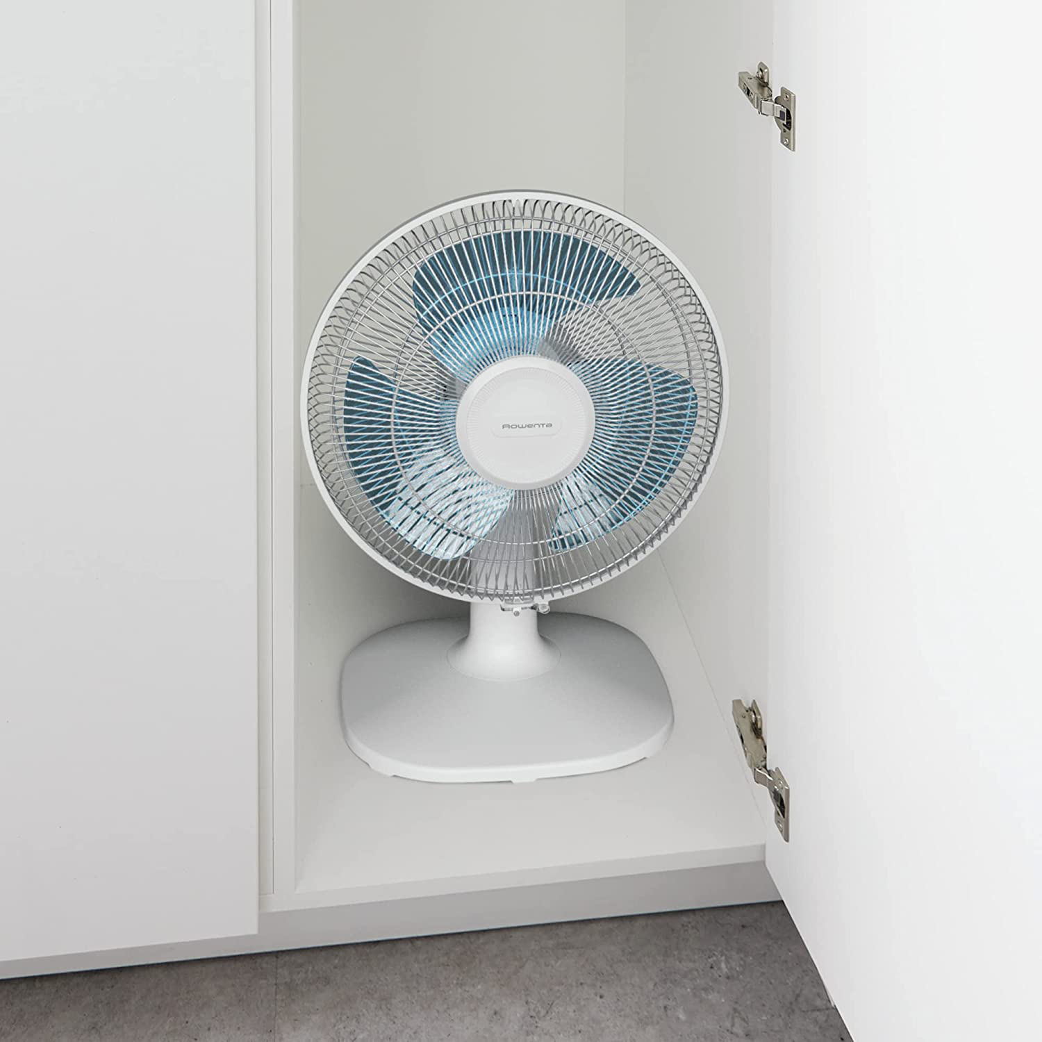 Ventilatore oscillante bianco posto all'interno di un armadio bianco, porte aperte.