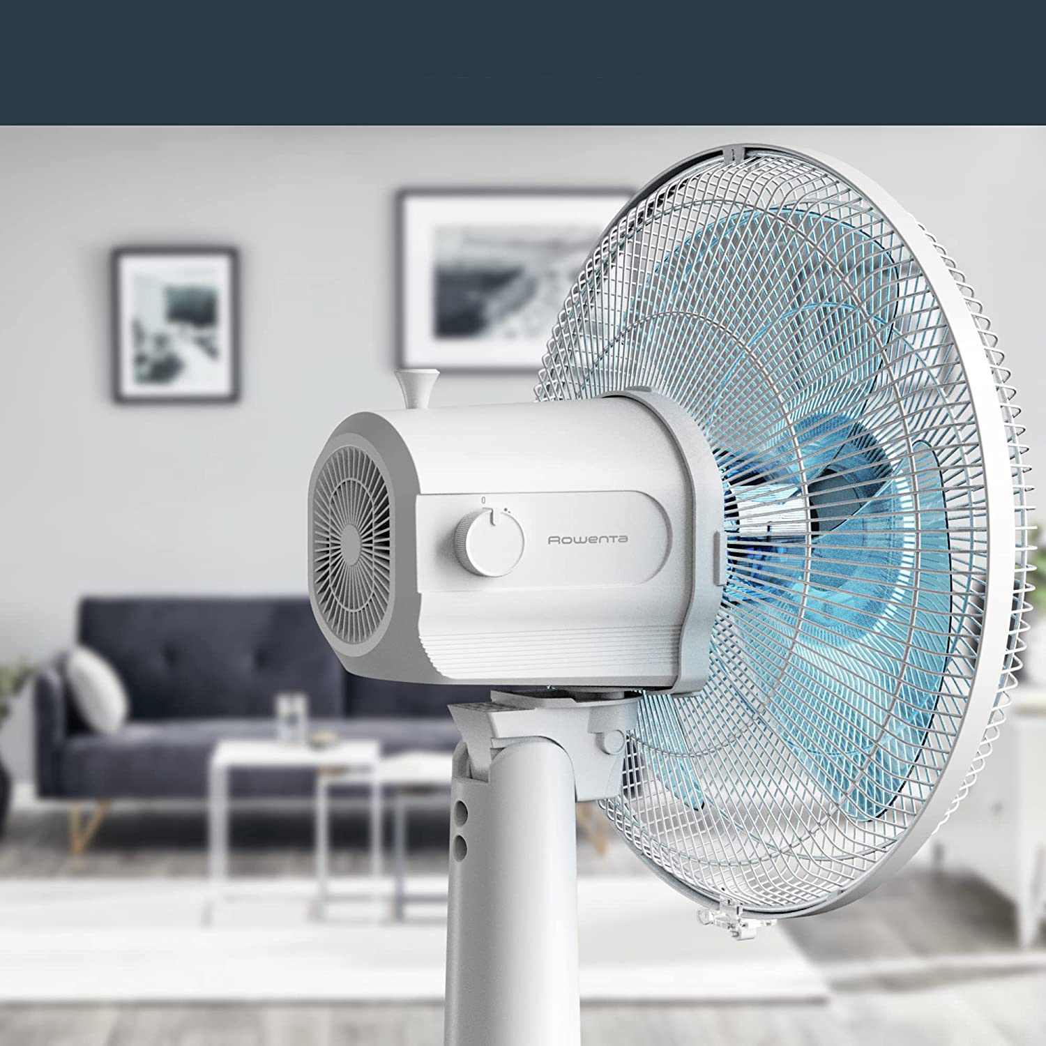Ventilatore bianco con pala blu. Il ventilatore è su un palo bianco. Lo sfondo è sfocato con vista stanza.