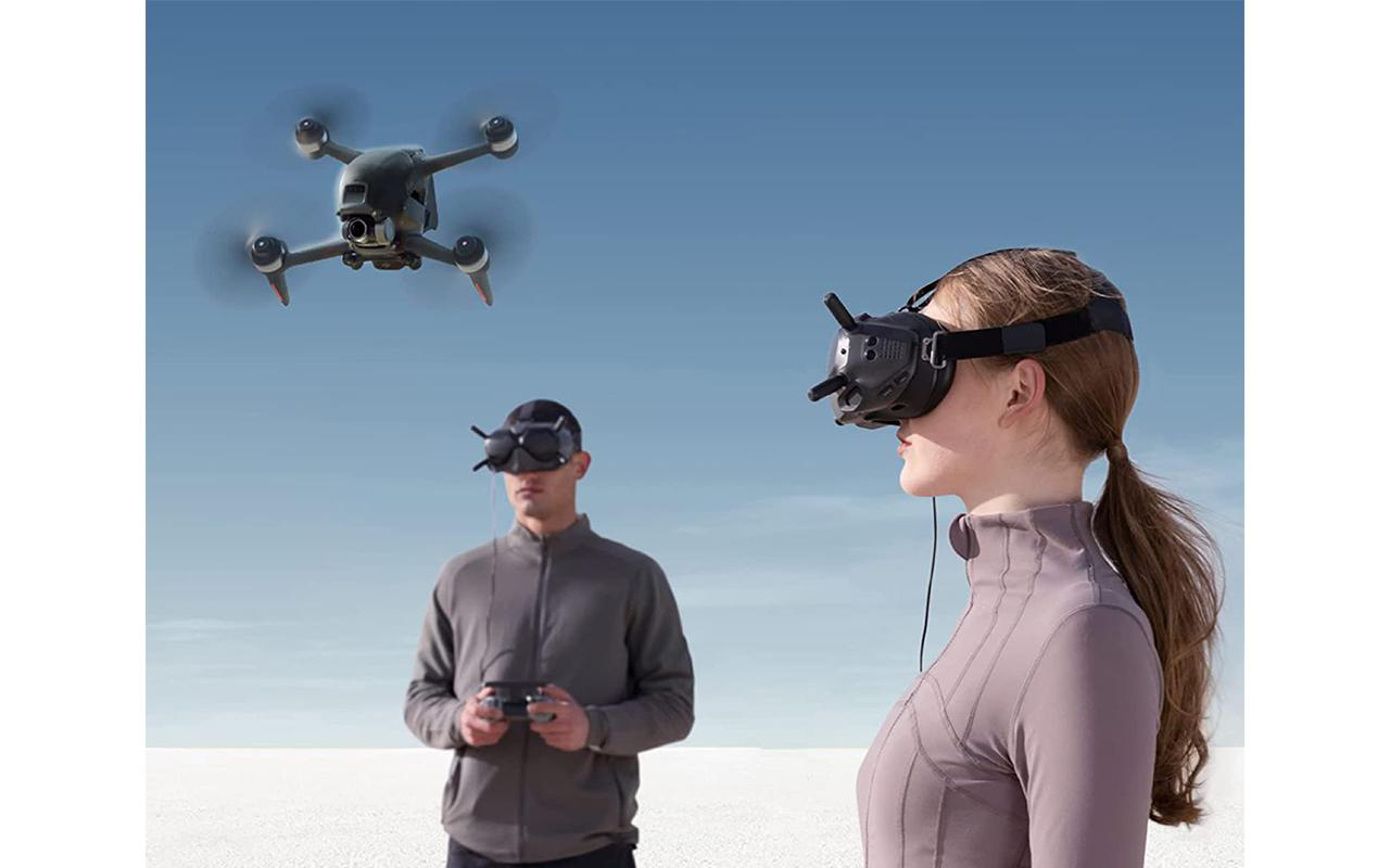 Personen, die VR-Headsets benutzen und Drohnen am Himmel fliegen. Eine Person hält einen Controller.
