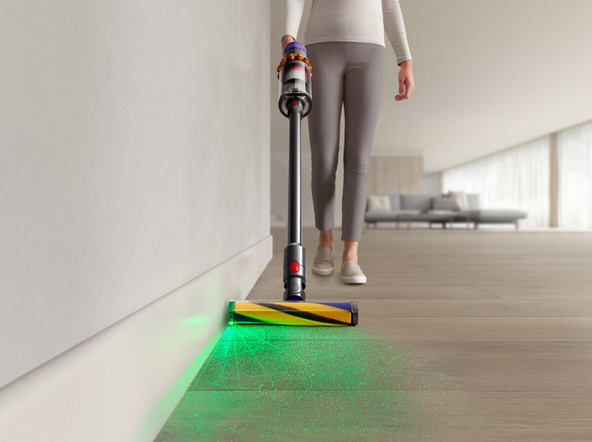 Osoba odkurzająca drewnianą podłogę odkurzaczem, z zielonym światłem. Tło jest białe.