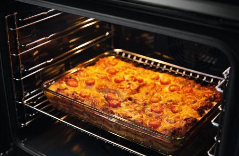 Szklane naczynie z ugotowaną lasagną z pomidorami w piekarniku.