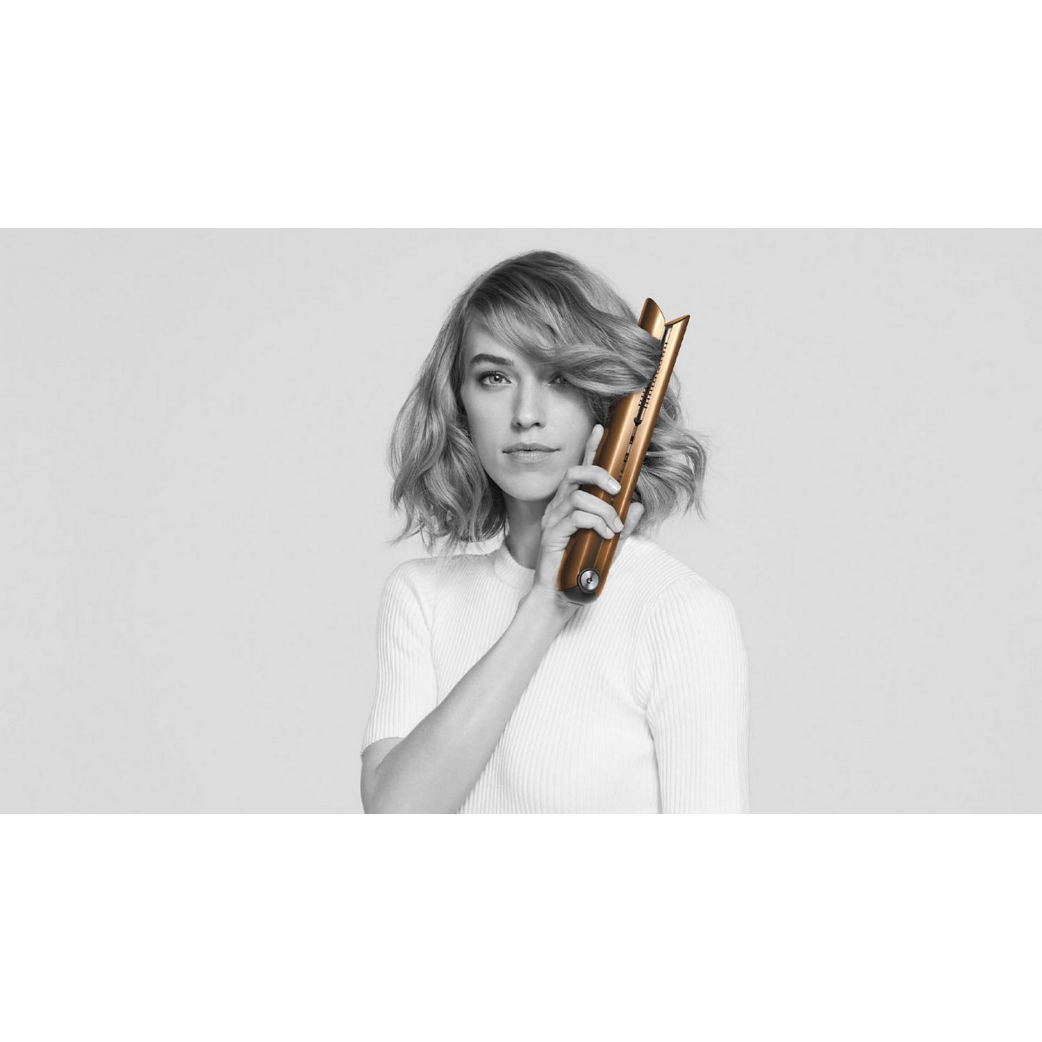 Woman holding a hair straightener, looking at camera on white background.