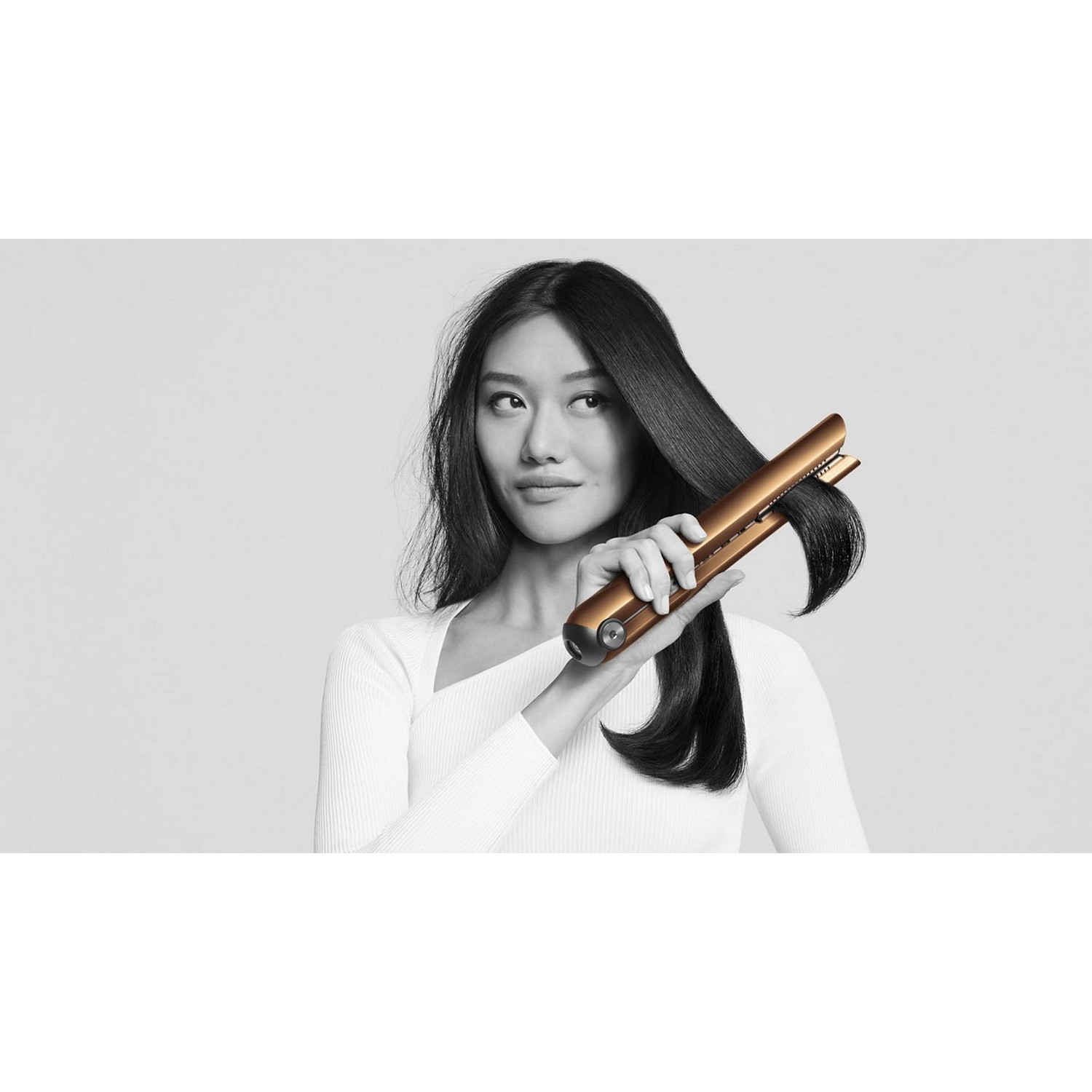 A woman is styling her hair with a gold hair straightener.