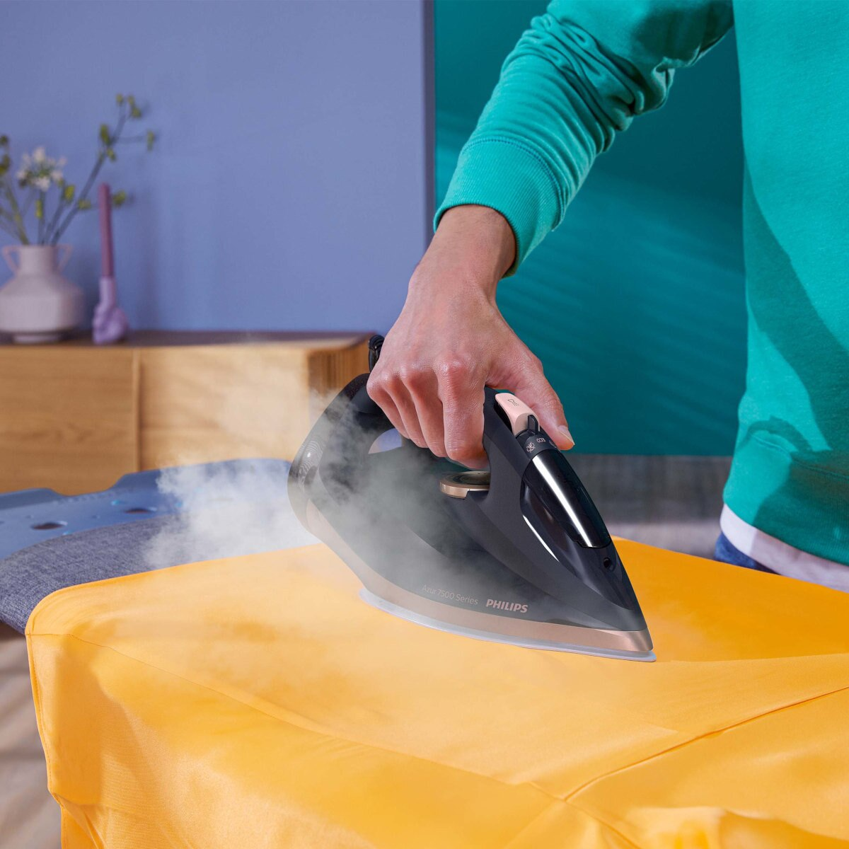 Osoba prasująca żółty element garderoby czarnym i srebrnym żelazkiem, widoczna para.