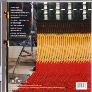 Rückseite einer Schallplattenhülle mit Songtiteln, Filmausrüstung und farbigen Bändern im Hintergrund.