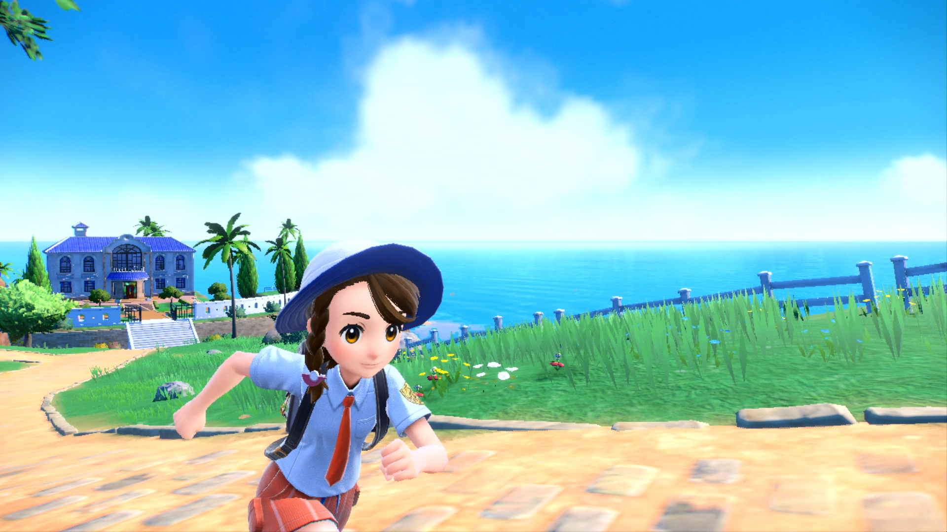 Girl running on a path towards a blue sea and sky with a building in the background.