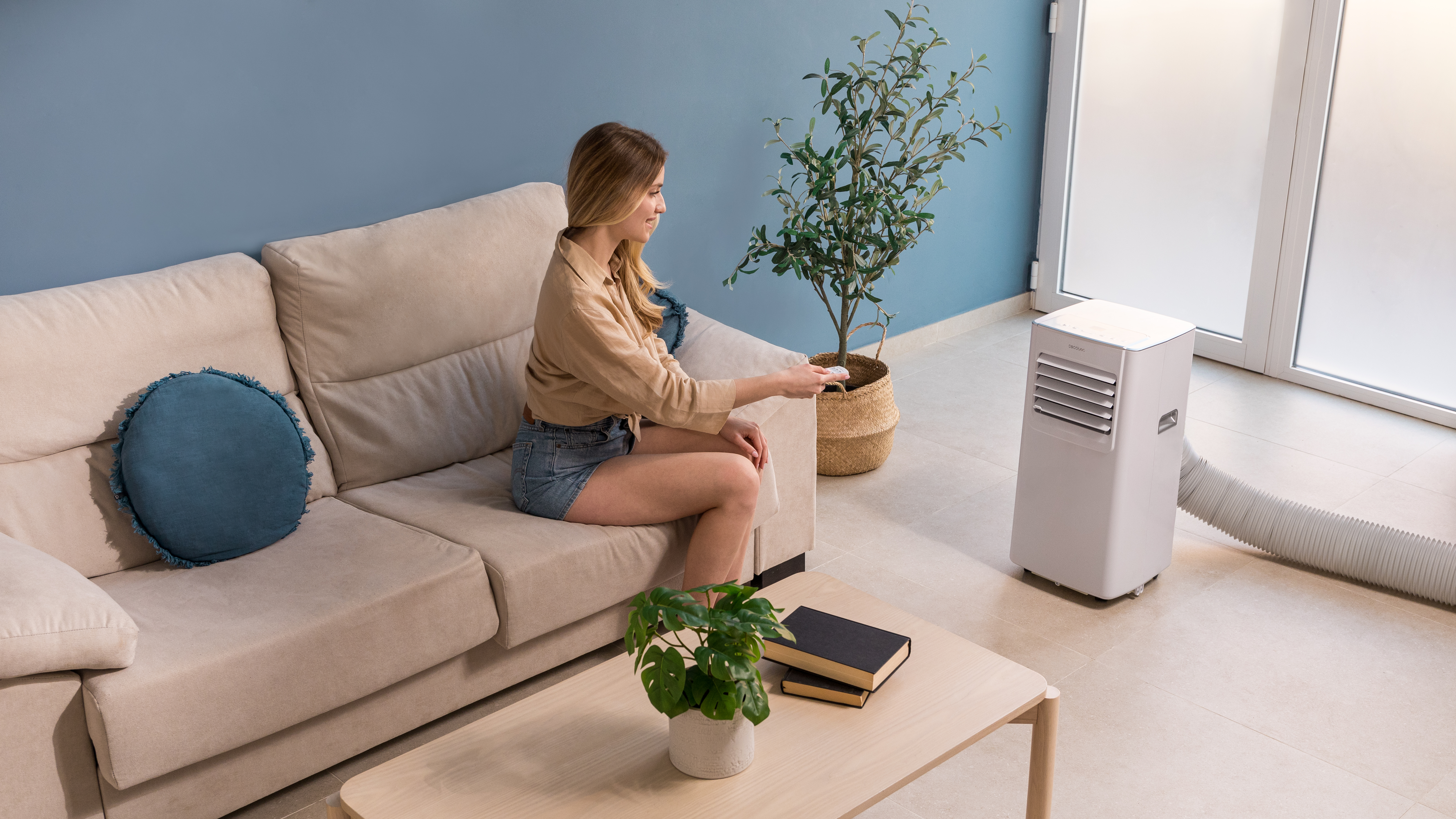 Mujer sentada en un sofá, usando un mando a distancia, junto a un AC.